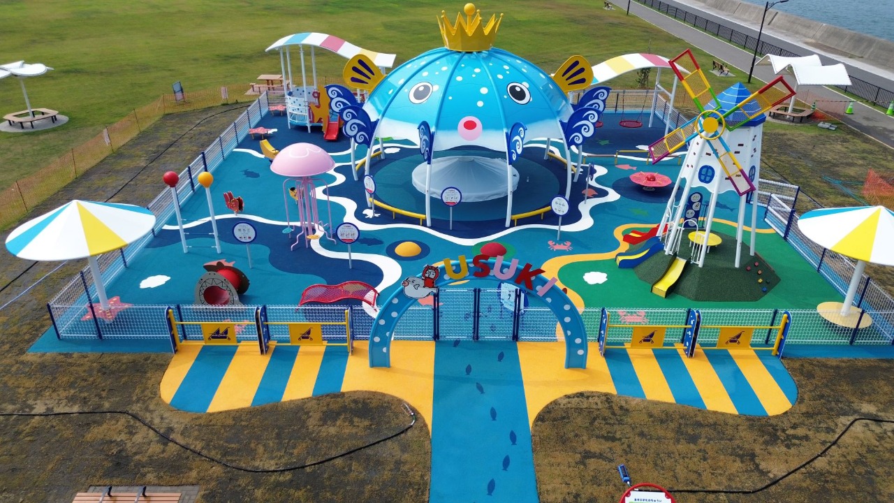 広い芝生広場や小さな子供が安心して遊べる遊具がある、海辺の眺望が楽しめる公園の写真。