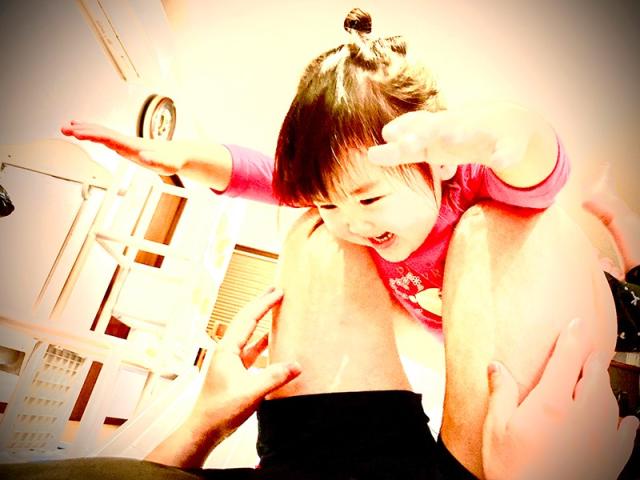 パパの脚にこどもが乗って飛行機遊びをしている画像